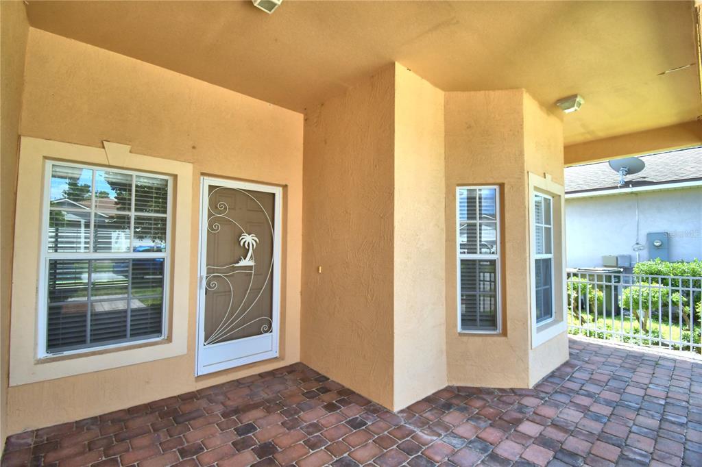 A covered patio features brick pavers, a white storm door, and several windows — 2338 SALZBURG LOOP, WINTER HAVEN, FL