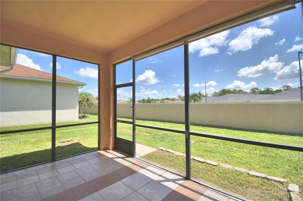 A tiled, screened-in patio overlooks a grassy backyard enclosed by a tan perimeter wall — 2338 SALZBURG LOOP, WINTER HAVEN, FL