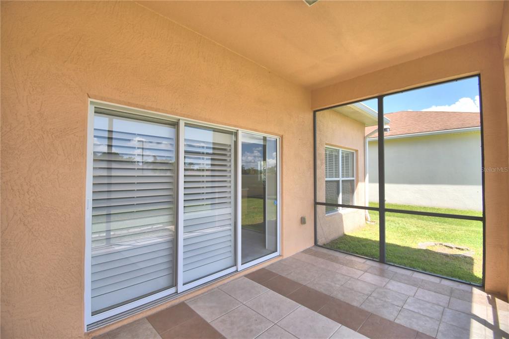 A covered patio with tiled flooring, a sliding glass door, and a screened-in wall — 2338 SALZBURG LOOP, WINTER HAVEN, FL