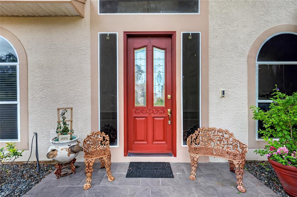 A red front door with glass panels sits between two windows on a tiled porch — 1920 EDGEWATER DRIVE, MOUNT DORA, FL