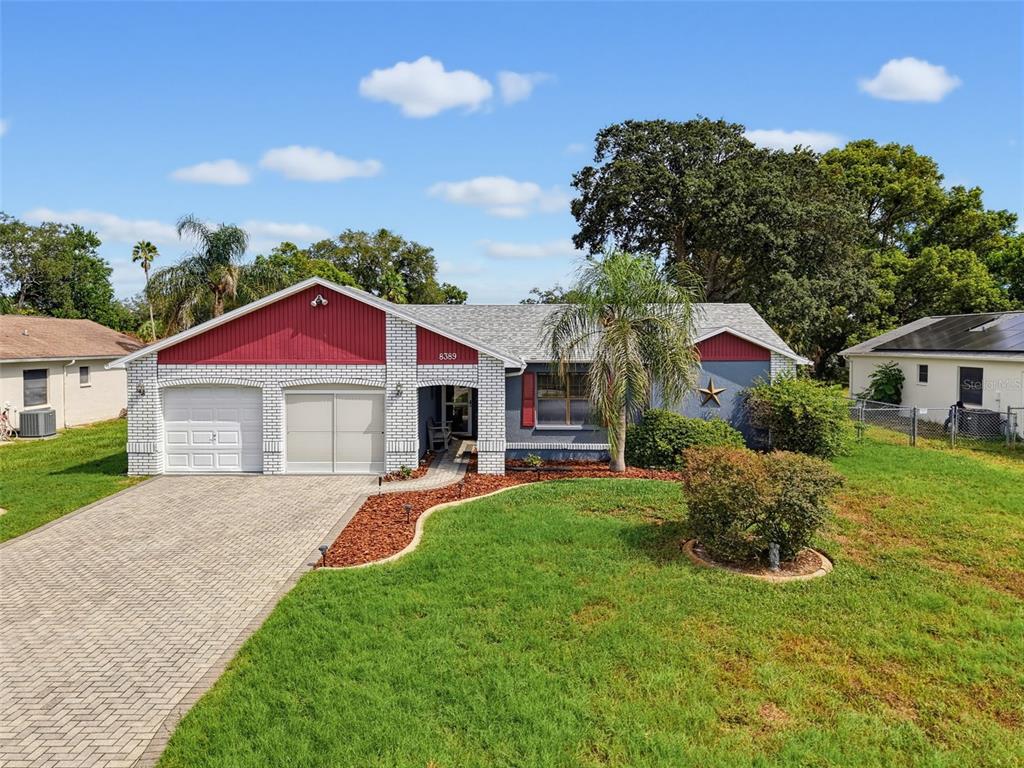 A single-story house with a brick facade, red gables, a paved driveway, and a front lawn — 8389 CAMPHOR DRIVE, SPRING HILL, FL