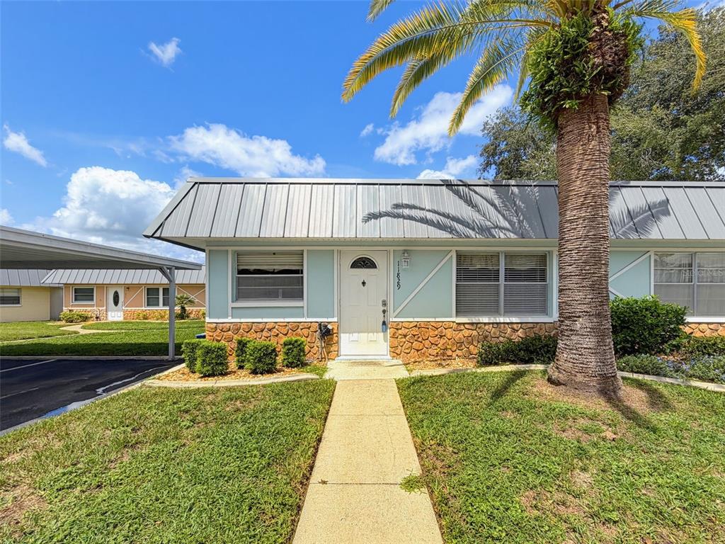 A single-story home with a metal roof, stone facade, and a palm tree in front — 11829 CARISSA LANE, NEW PORT RICHEY, FL