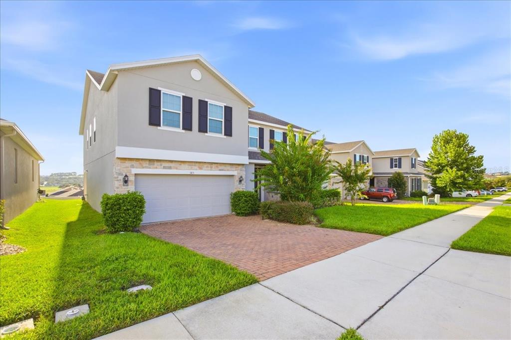 A two-story suburban house with a gray exterior, stone accents, and a brick driveway — 585 STERLING RESERVE WAY, MINNEOLA, FL