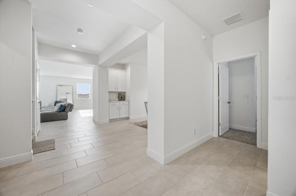 A bright hallway with light tile flooring leads to an open living area and kitchen — 585 STERLING RESERVE WAY, MINNEOLA, FL
