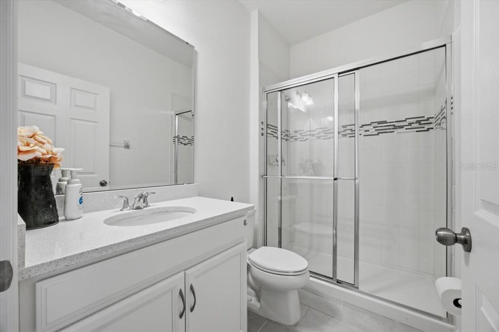 A bathroom with a white vanity, a mirror, a toilet, and a glass-enclosed shower — 585 STERLING RESERVE WAY, MINNEOLA, FL