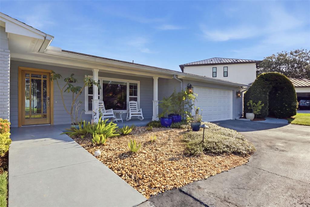 A gray single-story house features a wooden front door, a gravel garden, and a garage — 10715 CARROLLWOOD DRIVE, TAMPA, FL