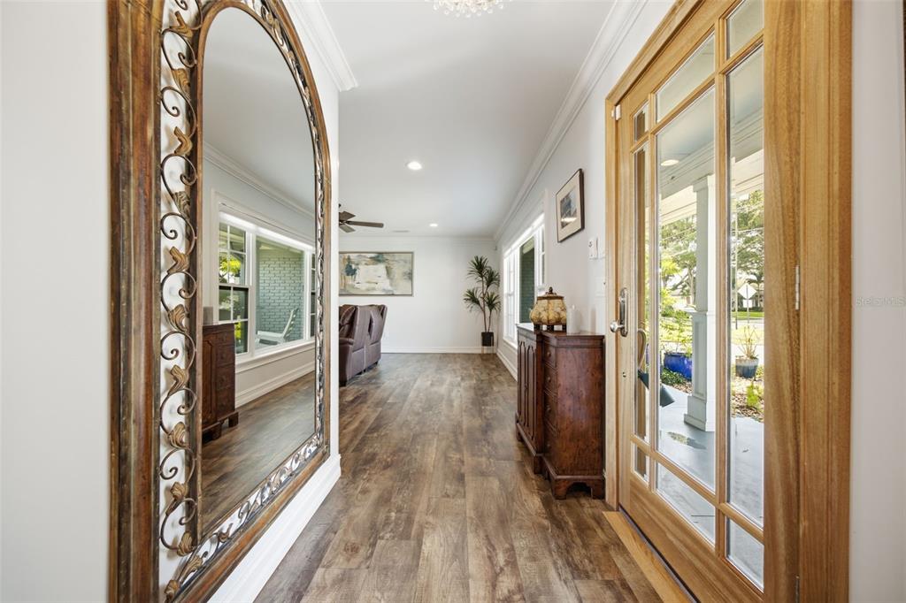 An entryway features wood-look flooring, a large arched mirror, and a glass-paneled wooden front door — 10715 CARROLLWOOD DRIVE, TAMPA, FL