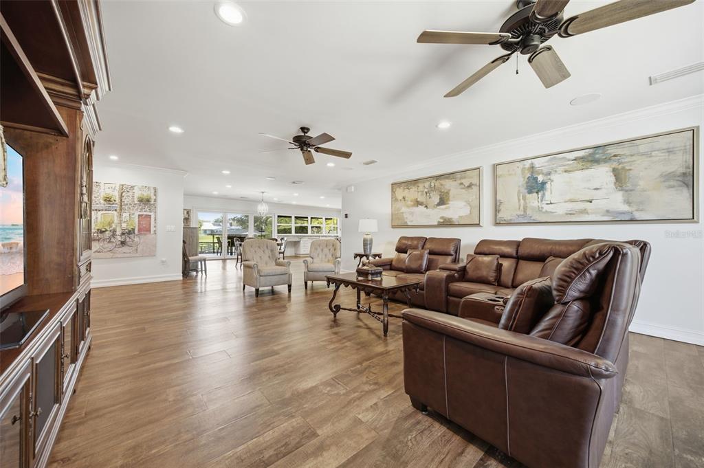 A spacious living room features brown leather furniture, wood-look tile flooring, and two ceiling fans — 10715 CARROLLWOOD DRIVE, TAMPA, FL