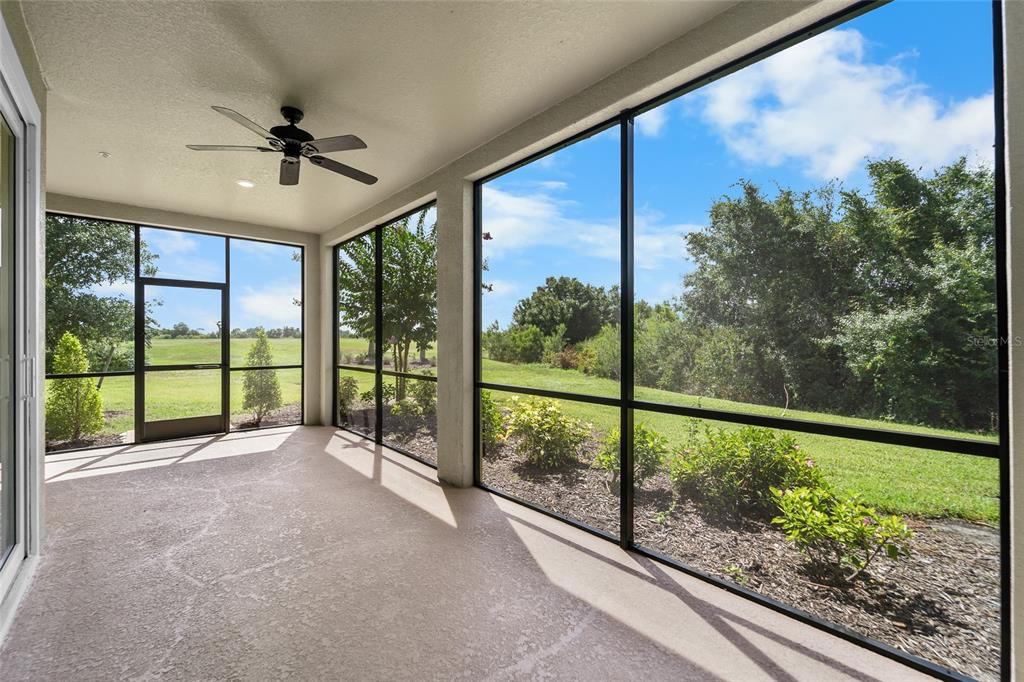 A screened-in patio with a ceiling fan overlooks a grassy yard and trees — 7342 DIVOT LOOP, LAKEWOOD RANCH, FL
