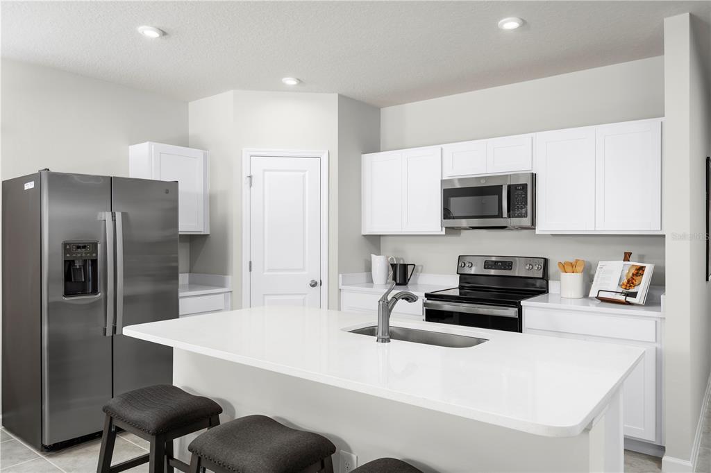 A kitchen features white cabinets, stainless steel appliances, and a white quartz-topped island with stools — 8890 WILDFLOWER FIELD LANE, WILDWOOD, FL