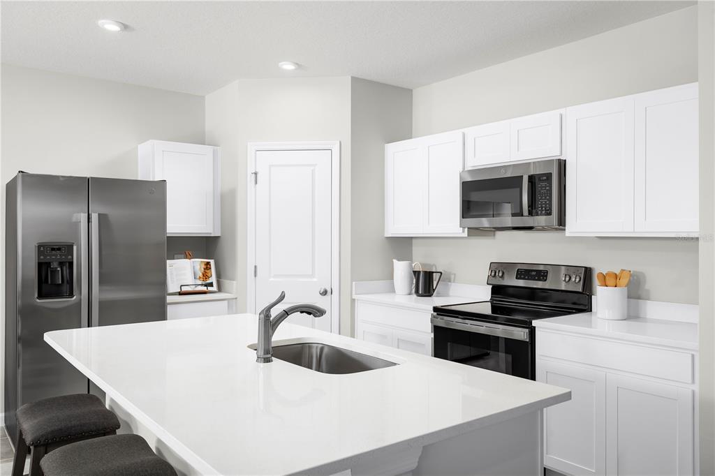 A modern kitchen features white cabinets, stainless steel appliances, a large island, and quartz countertops — 8890 WILDFLOWER FIELD LANE, WILDWOOD, FL