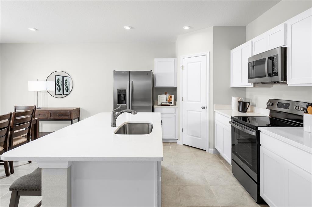A modern kitchen features a white island, stainless steel appliances, and white cabinetry — 8890 WILDFLOWER FIELD LANE, WILDWOOD, FL