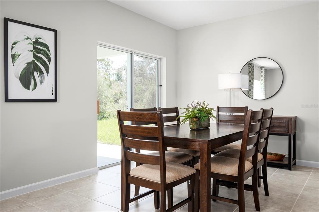 A dining room with a wooden table, four chairs, a sliding glass door, and wall art — 8890 WILDFLOWER FIELD LANE, WILDWOOD, FL