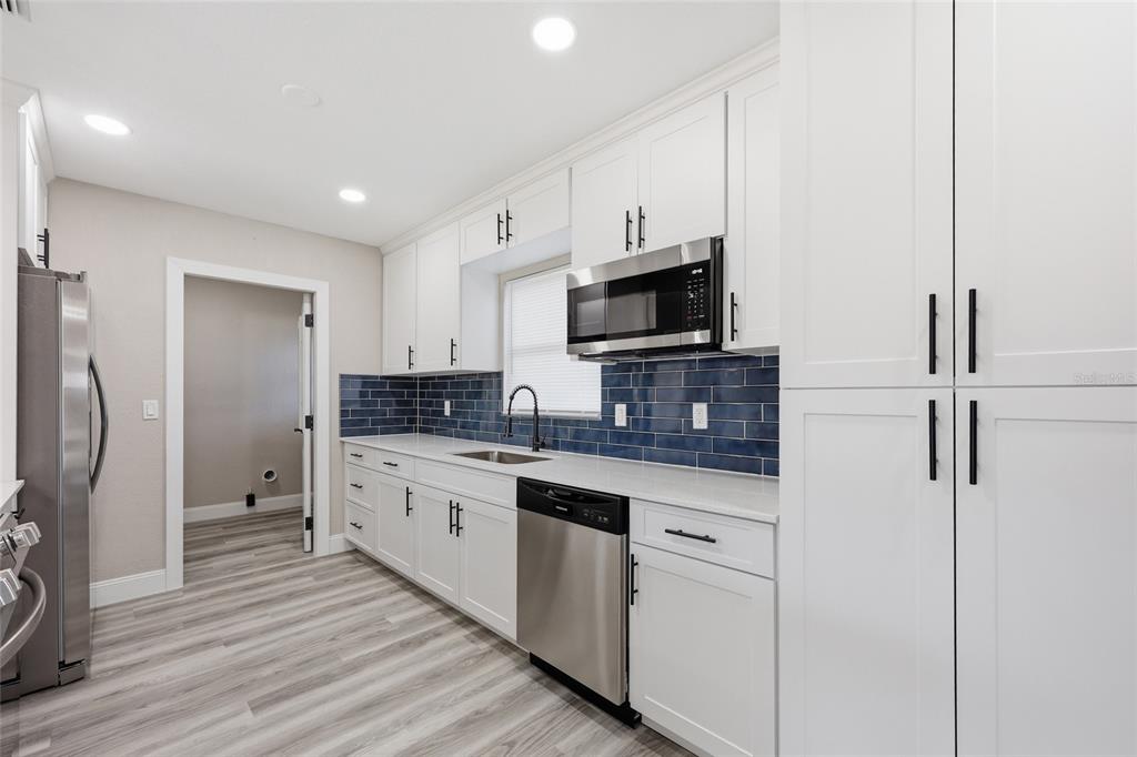 A bright open-concept kitchen and living area with wood-look flooring and white cabinetry — 1817 HUNT LANE, CLEARWATER, FL