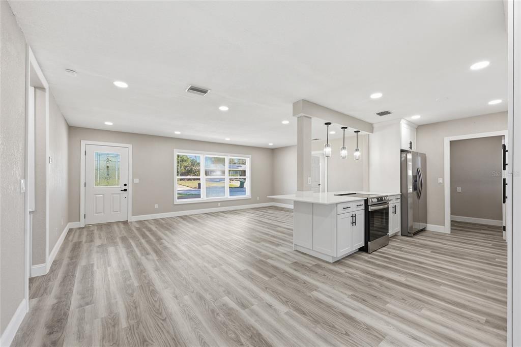 An open-concept kitchen with white cabinets and a breakfast bar overlooks a living area — 1817 HUNT LANE, CLEARWATER, FL