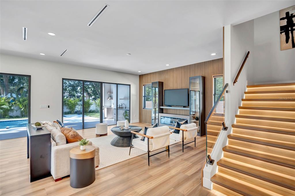 A modern living room features wood-slat walls, a staircase with illuminated steps, and sliding glass doors — 2112 W FARWELL DRIVE, TAMPA, FL
