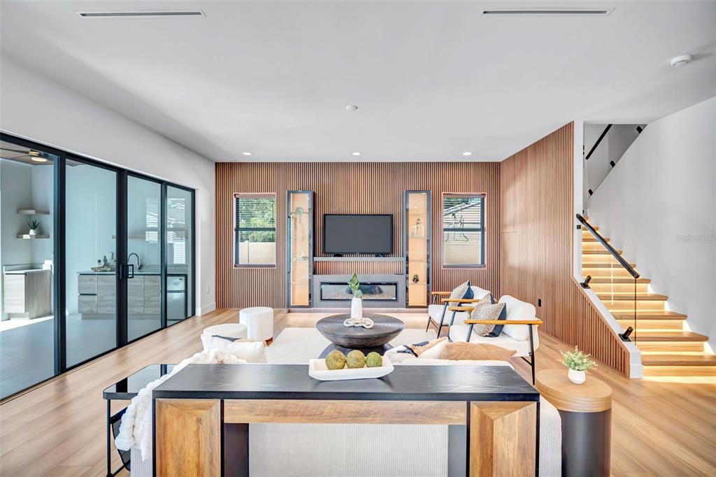 A modern living room features wood-slat walls, a fireplace, and a staircase with illuminated steps — 2112 W FARWELL DRIVE, TAMPA, FL