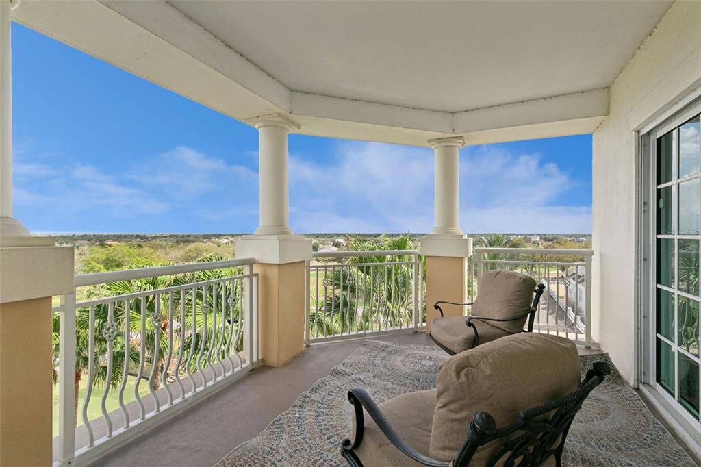 A covered balcony features two armchairs, a patterned rug, white railings, and scenic outdoor views — 7593 GATHERING DRIVE UNIT 401, REUNION, FL