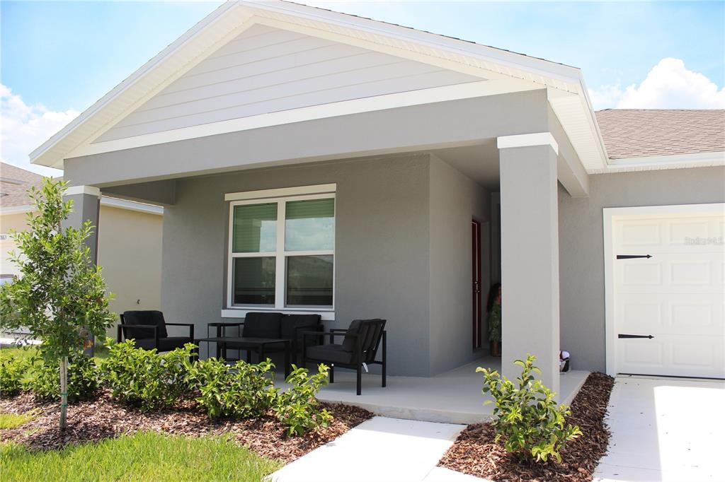 A gray single-story house exterior features a covered porch with outdoor furniture and a garage — 2869 HOUSE FINCH ROAD, ST CLOUD, FL