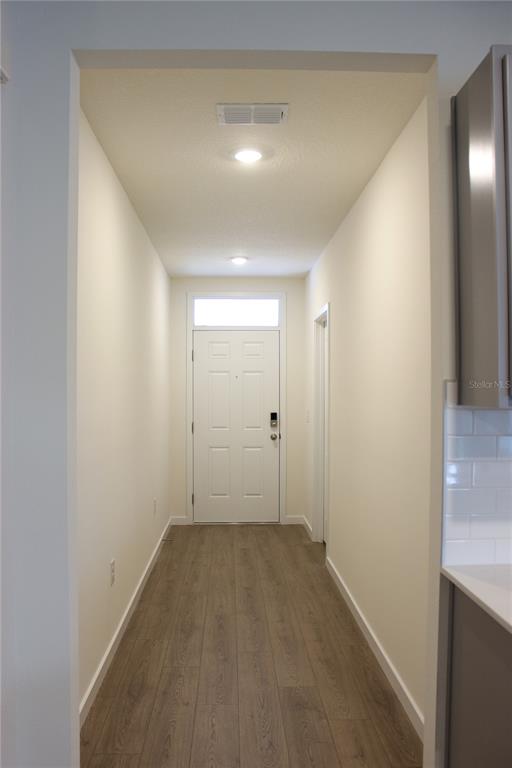 A hallway with wood-look flooring leads to a white front door with a transom window — 2869 HOUSE FINCH ROAD, ST CLOUD, FL