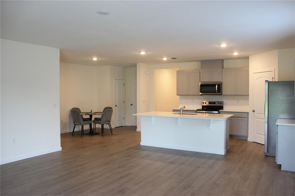 An open-concept kitchen features a white island, gray cabinetry, and light wood-look flooring — 2869 HOUSE FINCH ROAD, ST CLOUD, FL