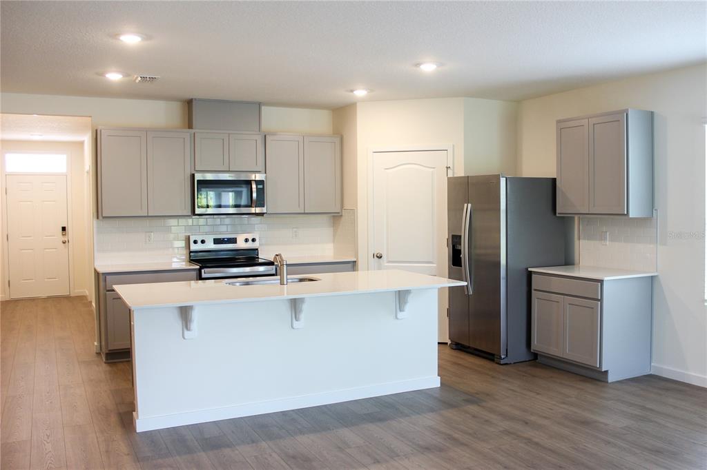 A kitchen features gray cabinets, white countertops, a central island, and stainless steel appliances — 2869 HOUSE FINCH ROAD, ST CLOUD, FL