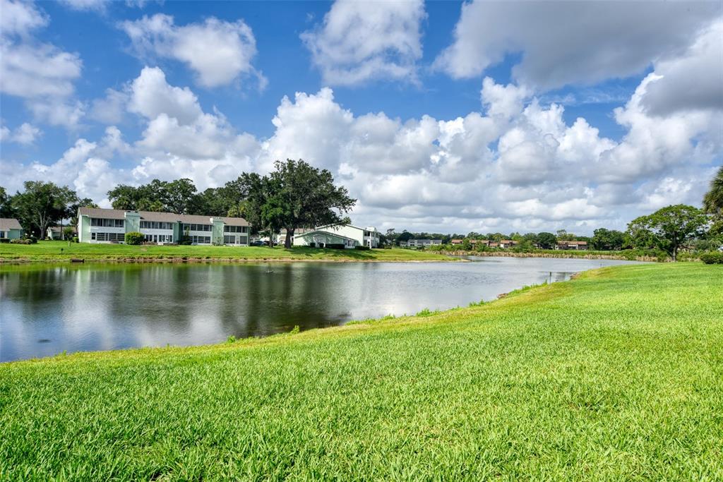 A grassy lawn overlooks a pond with apartment buildings in the background under a cloudy sky — 519 MIDWAY DRIVE UNIT A, OCALA, FL