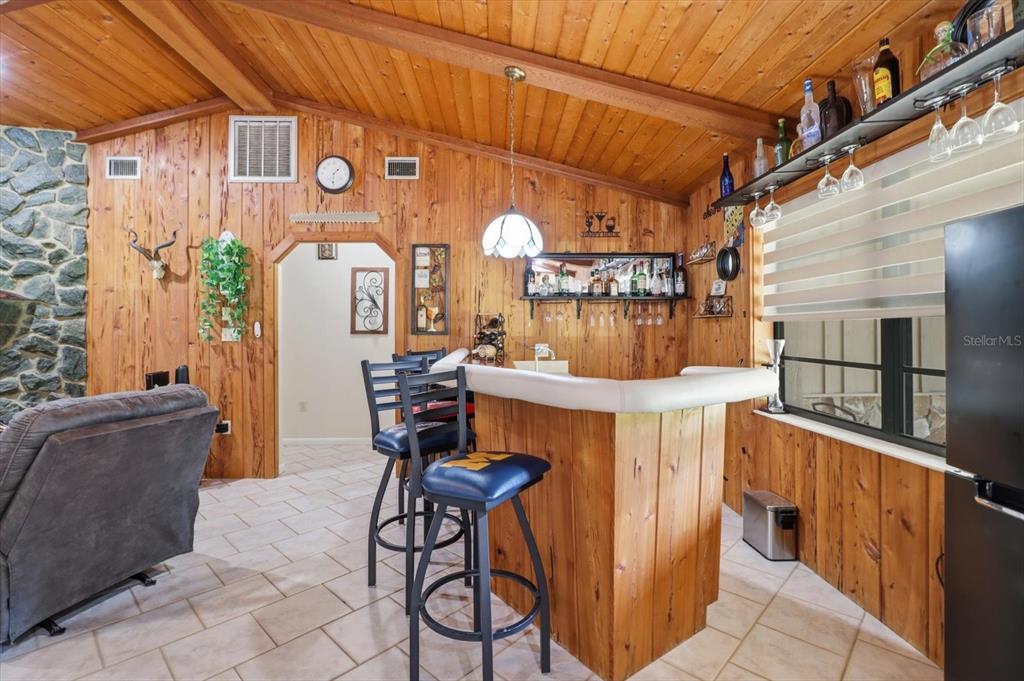 A rustic room features wood-paneled walls, a built-in bar with stools, and a stone fireplace — 10265 W SPRINGTREE LANE, CRYSTAL RIVER, FL