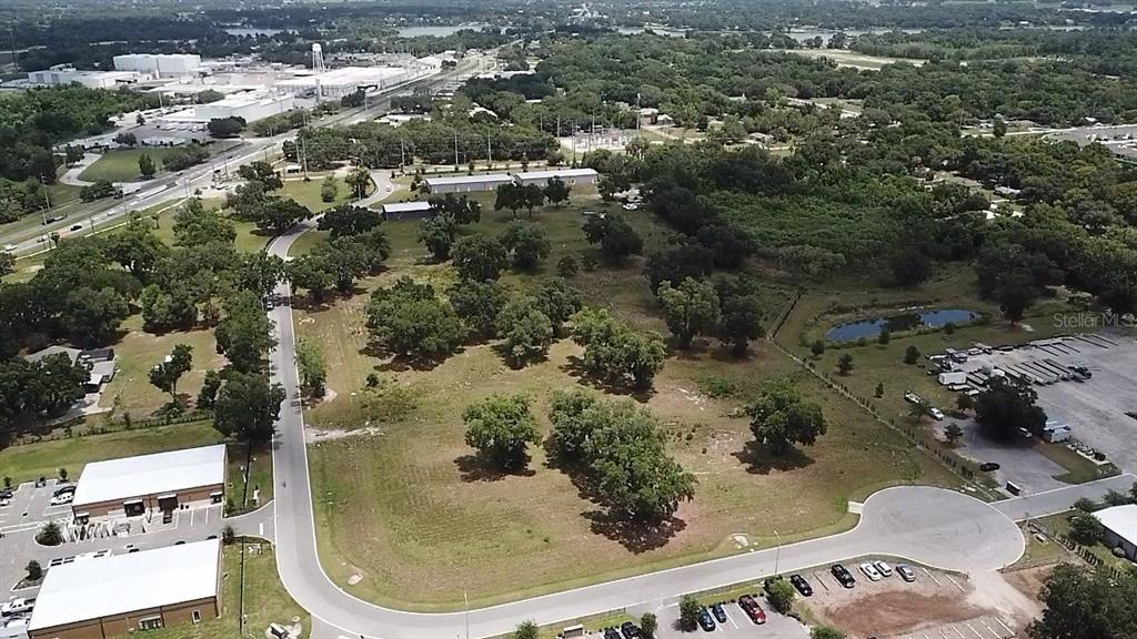 An aerial view shows a vacant grassy lot surrounded by trees, roads, and commercial buildings — 1060 DUCK BOX ROAD, UMATILLA, FL