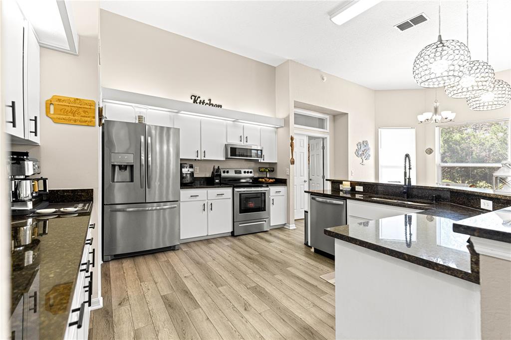 A kitchen features white cabinetry, stainless steel appliances, dark granite countertops, and light wood flooring — 6744 SW 113TH PLACE, OCALA, FL