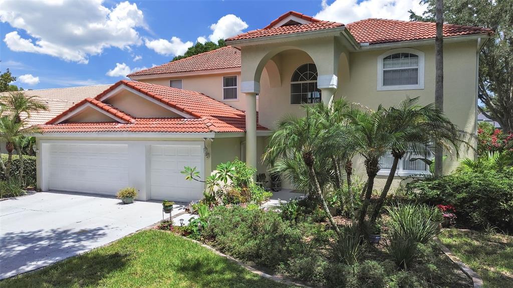 A two-story house with a red tile roof, white garage doors, and a landscaped front yard — 10212 GARDEN ALCOVE DRIVE, TAMPA, FL