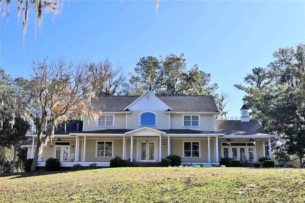 A two-story yellow house with a wrap-around porch sits on a grassy, tree-lined lot — 15551 NW HIGHWAY 225, REDDICK, FL