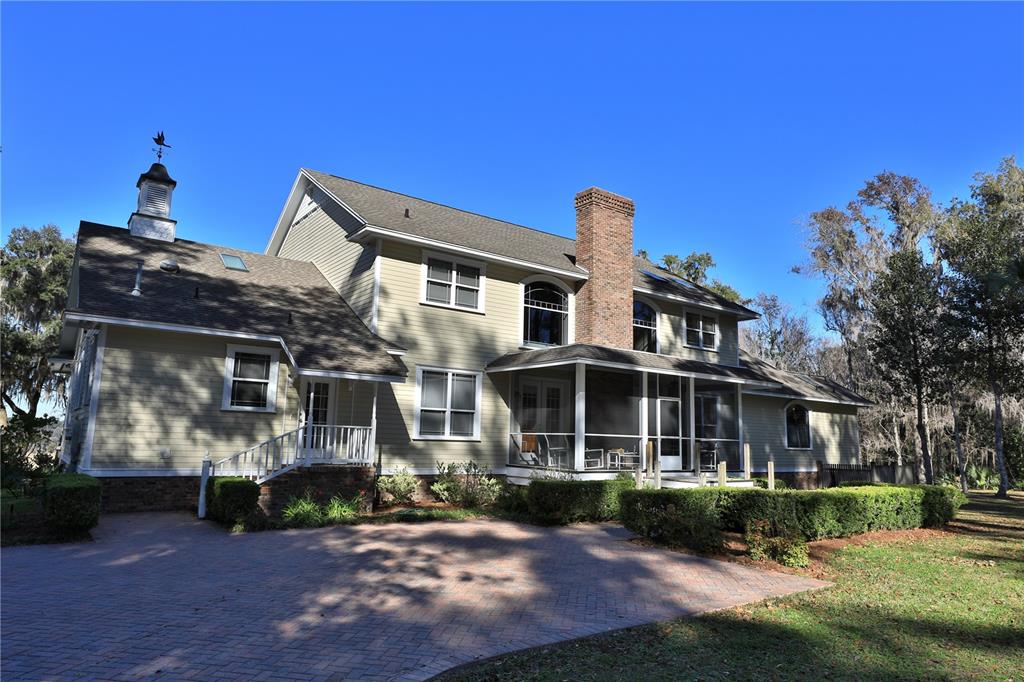 A two-story house with light siding, a brick chimney, and a screened-in porch — 15551 NW HIGHWAY 225, REDDICK, FL