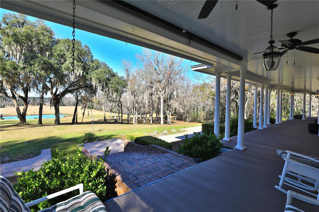 A covered porch with white columns overlooks a brick patio, lawn, and a pond — 15551 NW HIGHWAY 225, REDDICK, FL
