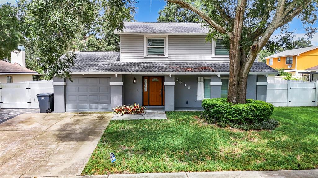 A two-story house with gray siding, a single-car garage, and a large tree in front — 12438 CARDIFF DRIVE, TAMPA, FL