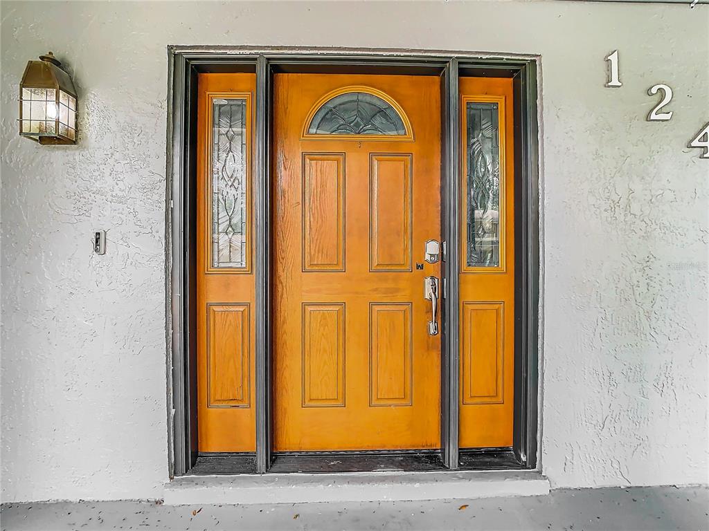 A wooden front door with a glass arched window and sidelights sits on a stucco wall — 12438 CARDIFF DRIVE, TAMPA, FL