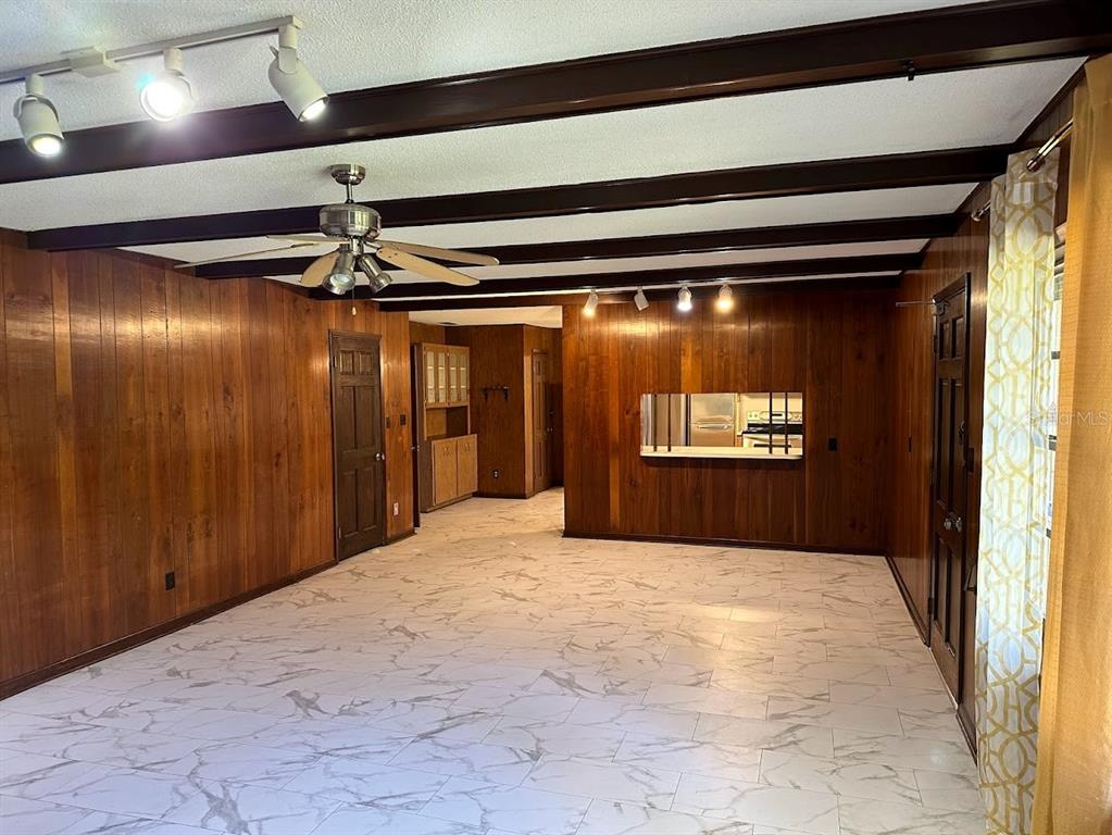 A living room features wood-paneled walls, exposed ceiling beams, a ceiling fan, and marble-look tile — 1333 SE 17TH STREET, OCALA, FL