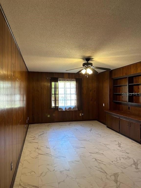 A room with wood-paneled walls, a ceiling fan, built-in shelving, and white marble-look tile flooring — 1333 SE 17TH STREET, OCALA, FL
