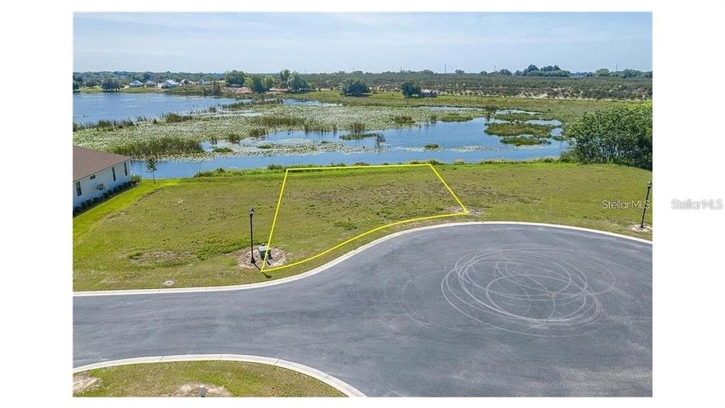 An aerial view shows a vacant residential lot outlined in yellow next to a lake — 116 N CALADIUM AVENUE, LAKE ALFRED, FL