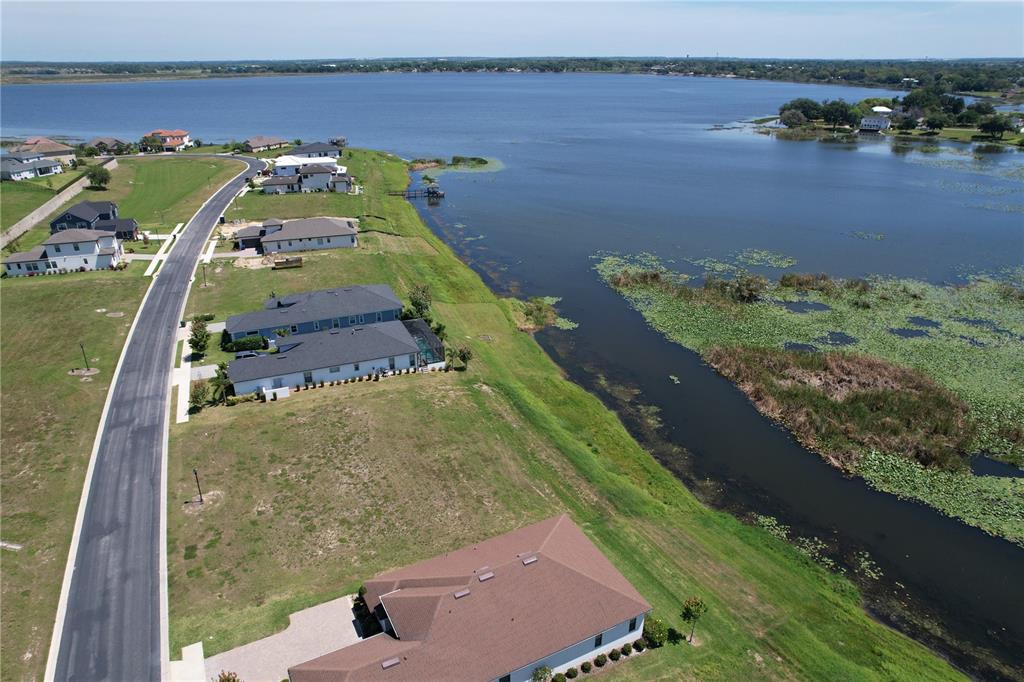 An aerial view shows houses along a road bordering a large lake with vegetation — 116 N CALADIUM AVENUE, LAKE ALFRED, FL