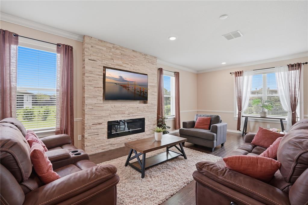 A living room features a stone fireplace, a wall-mounted television, brown leather furniture, and windows — 9307 PARISIAN COURT, SEFFNER, FL