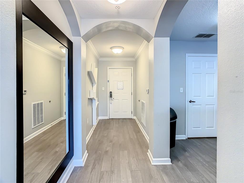 A hallway with light wood-look flooring, a large wall mirror, and an arched entryway — 14501 GROVE RESORT AVE UNIT 1707, WINTER GARDEN, FL