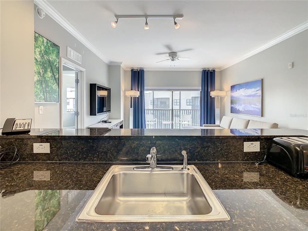 A kitchen sink with dark granite countertops overlooks a living room with a balcony view — 14501 GROVE RESORT AVE UNIT 1707, WINTER GARDEN, FL