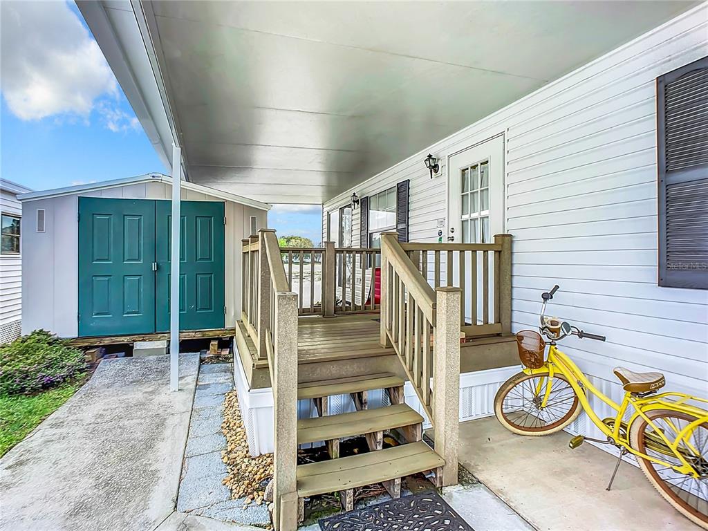 A wooden deck with stairs sits beside a mobile home with a yellow bicycle parked nearby — 92 EAGLE POINT S, OSTEEN, FL