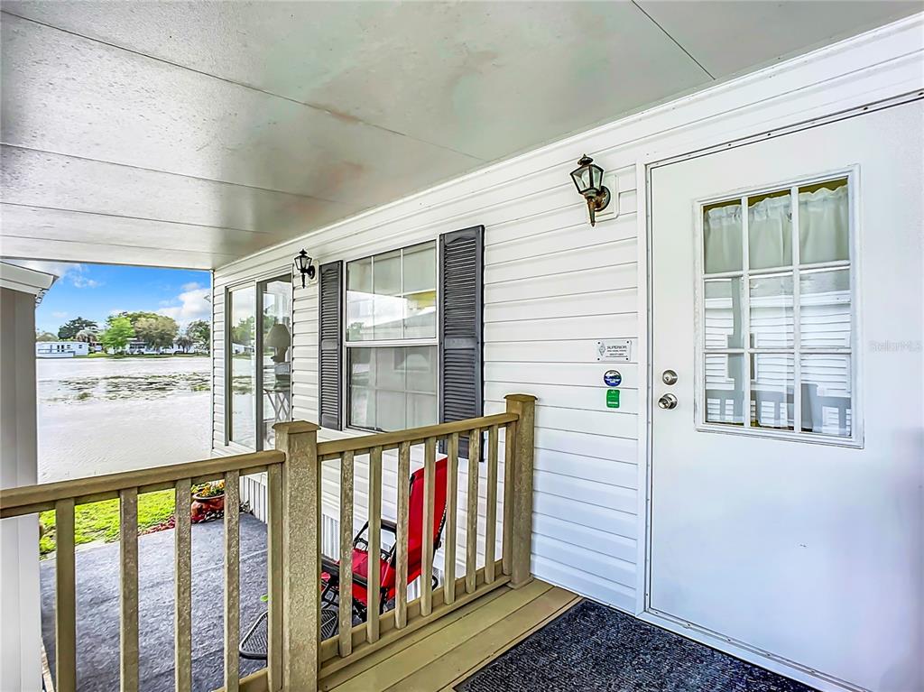 A covered porch with a wooden railing overlooks a lake next to a white house — 92 EAGLE POINT S, OSTEEN, FL