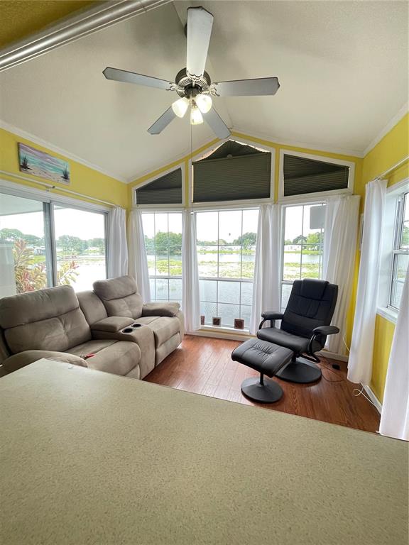 A sunroom with yellow walls, a ceiling fan, a sofa, and a chair overlooking water — 92 EAGLE POINT S, OSTEEN, FL