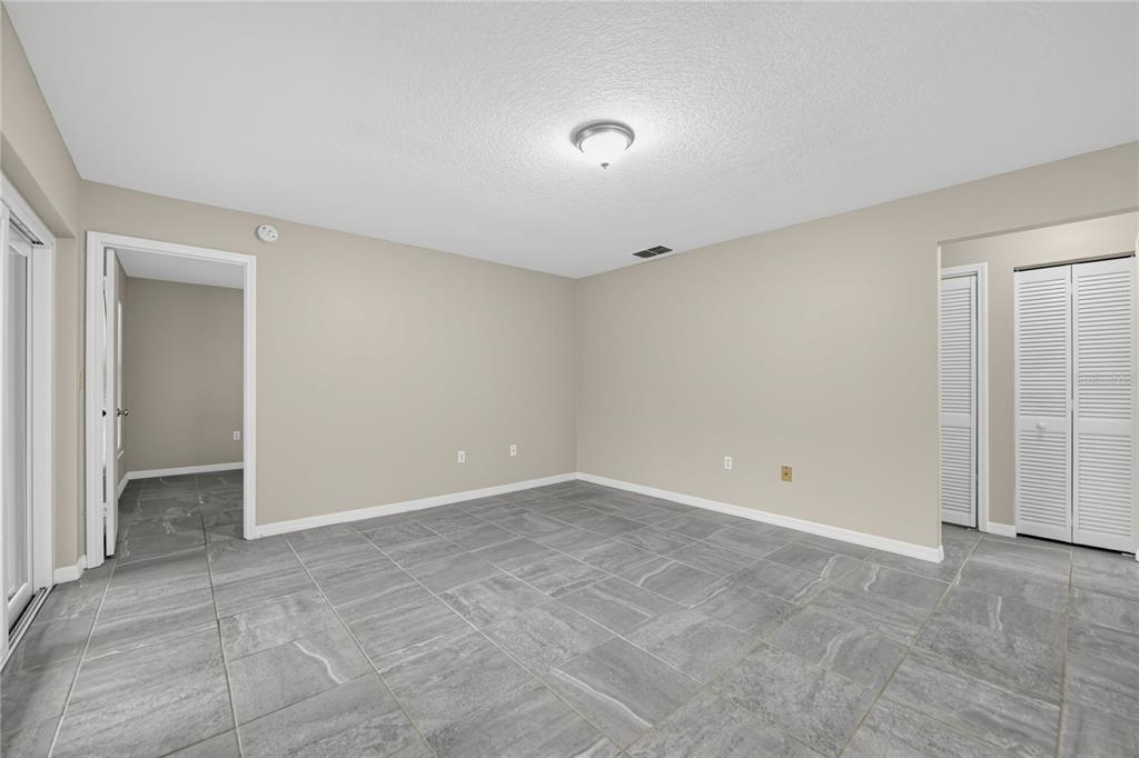 An empty room with gray tile flooring, beige walls, and white louvered closet doors — 523 HUNTER CIRCLE, KISSIMMEE, FL