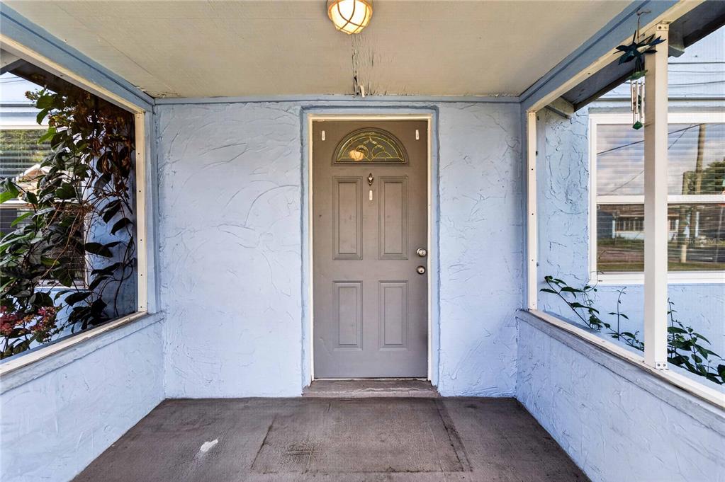 A covered front porch with light blue stucco walls, a gray door, and screened windows — 1103 BRACK STREET, KISSIMMEE, FL