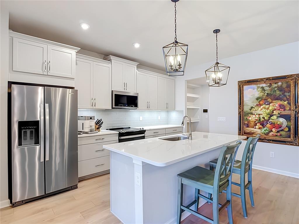 A modern kitchen features white cabinetry, stainless steel appliances, a quartz island, and two pendant lights — 2376 AUDUBON PRESERVE LANE, LUTZ, FL