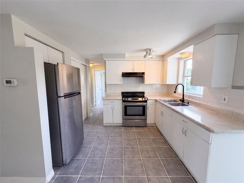A kitchen features white cabinets, stainless steel appliances, a double sink, and gray tiled flooring — 4718 TRAFFORD ROAD, HOLIDAY, FL